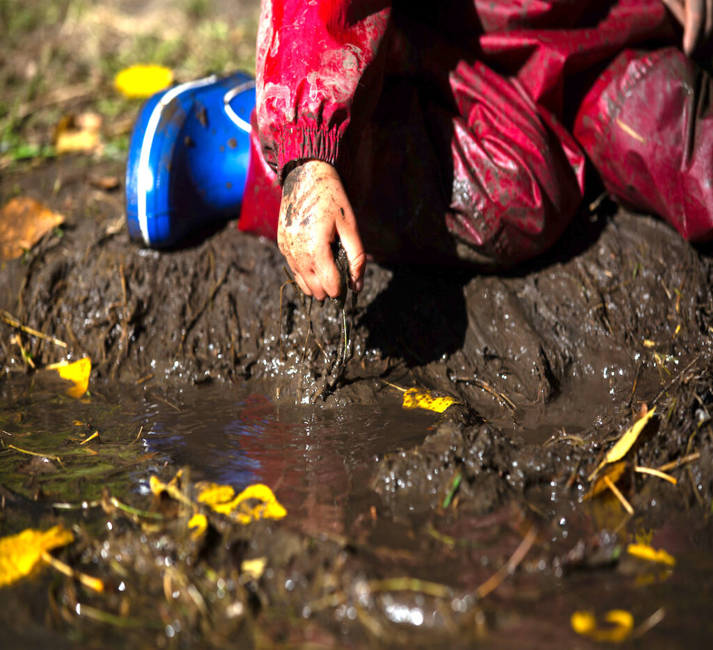 close up of child exploring mud in rain gear