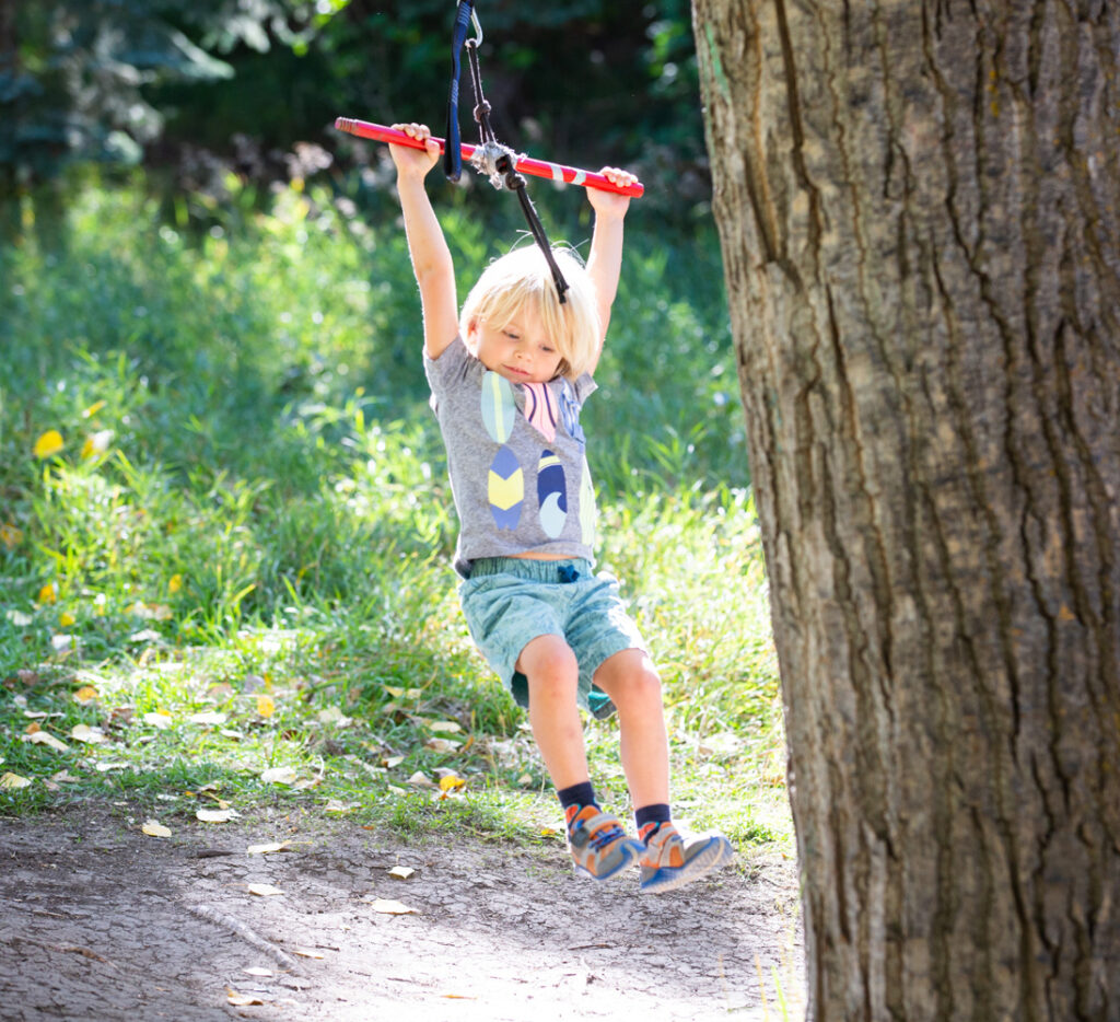 Child swinging on outdoor play ropes in the forest