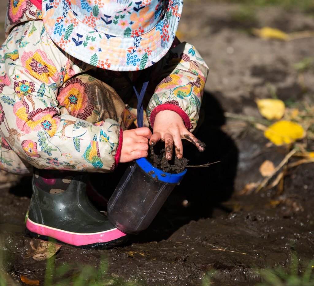 child exploring in the mud in rain gear